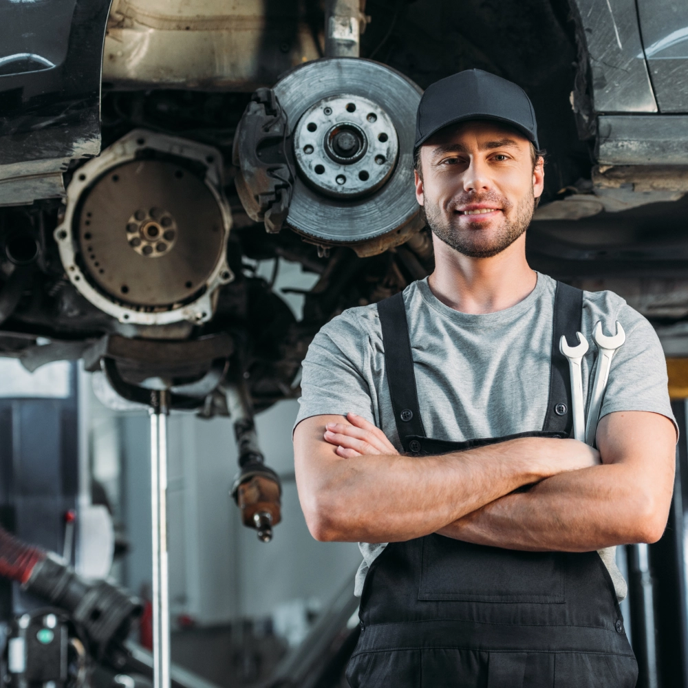 A man standing under an automobile with his arms crossed.