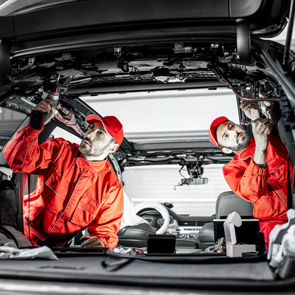 Two people in red jackets working on a car.