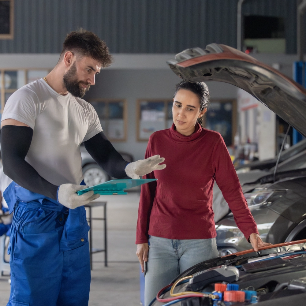 A man and woman looking at the car in a garage.