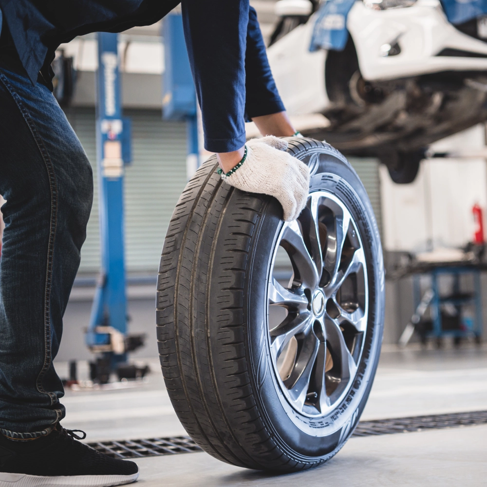 A person holding a tire in front of a car.